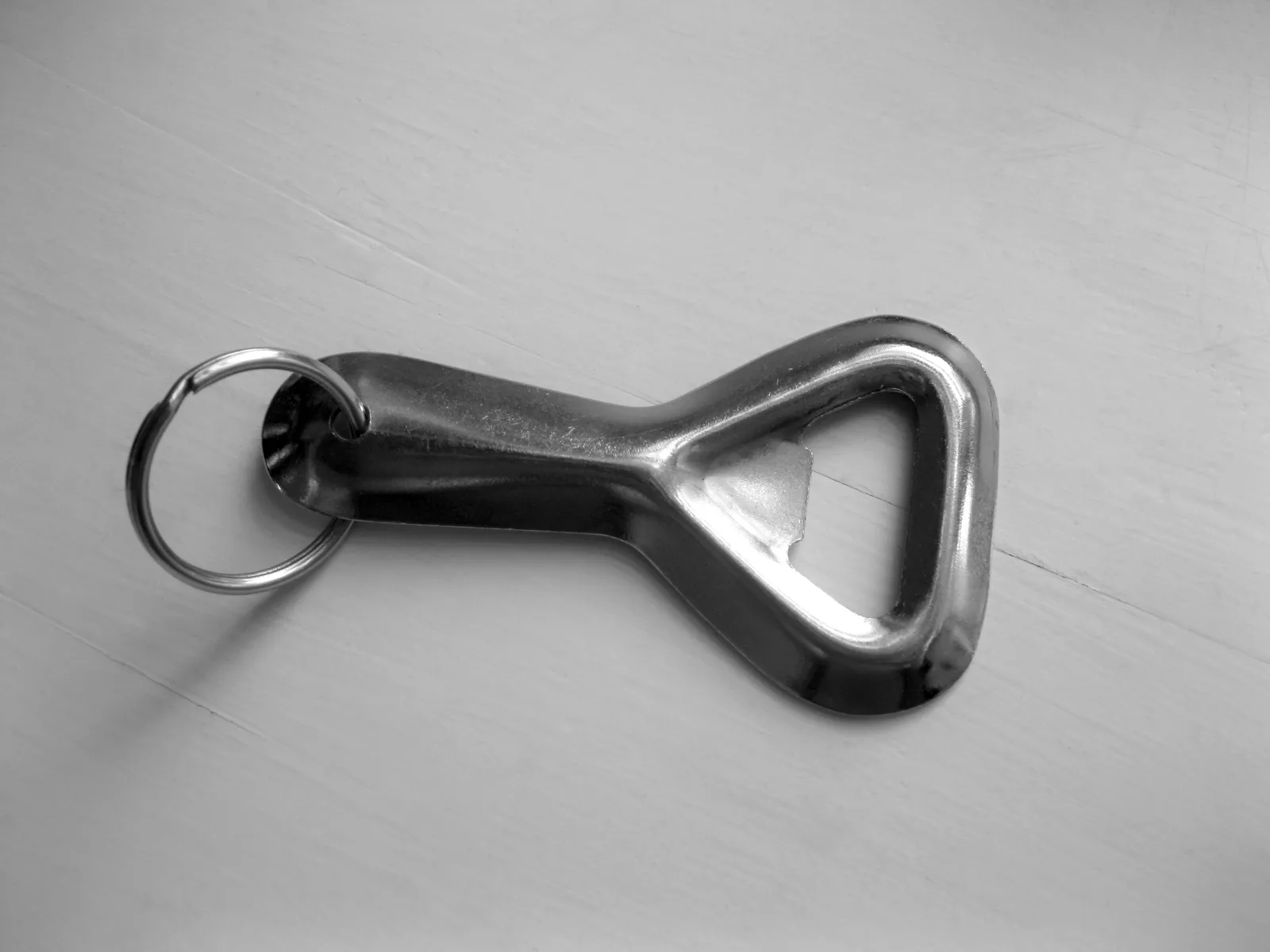 Décapsuleur de poche en métal brillant accroché à un anneau de porte-clés, posé sur une table blanche