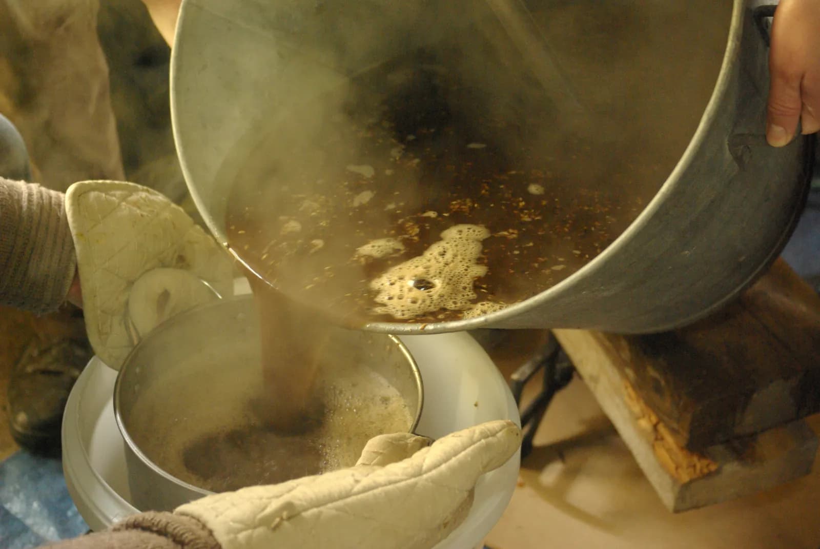Brassage amateur : deux mains gantées versent le moût d'une grande marmite dans une passoire posée sur un seau de fermentation
