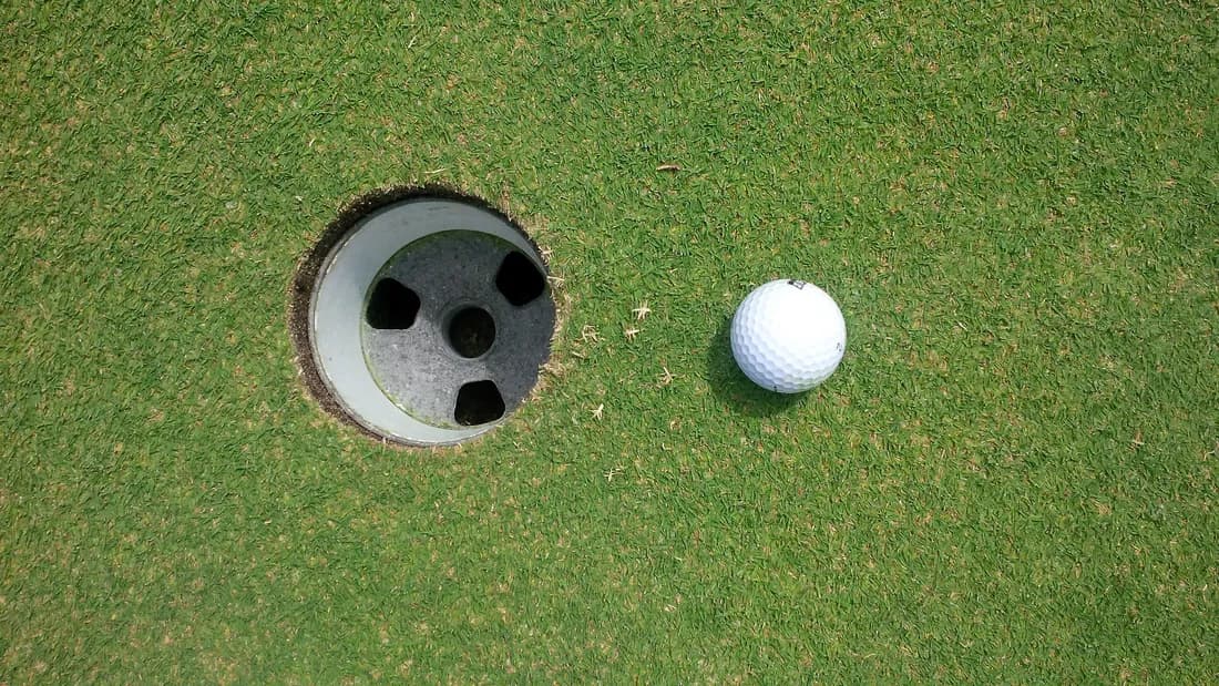 Balle de golf blanche arrêtée sur le green, à quelques centimètres du trou