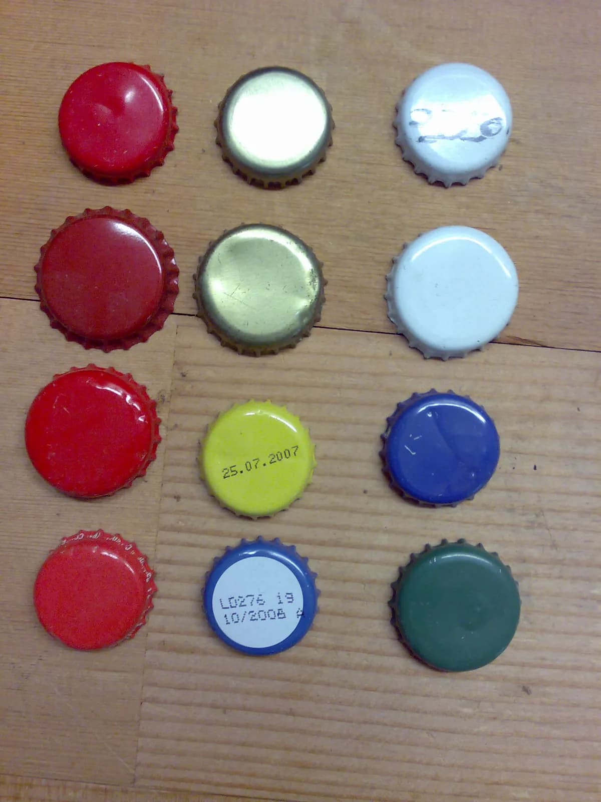 Douze capsules de bouteille dentelées, sans marque, rouges, dorées, blanches, jaunes, bleues et vertes, alignées sur une table en bois