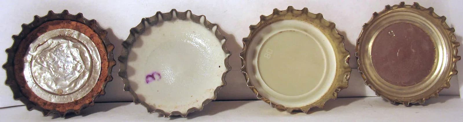 Quatre capsules de bouteille retournées côte à côte, montrant leurs joints intérieurs : liège et aluminium, blanc, crème et brun