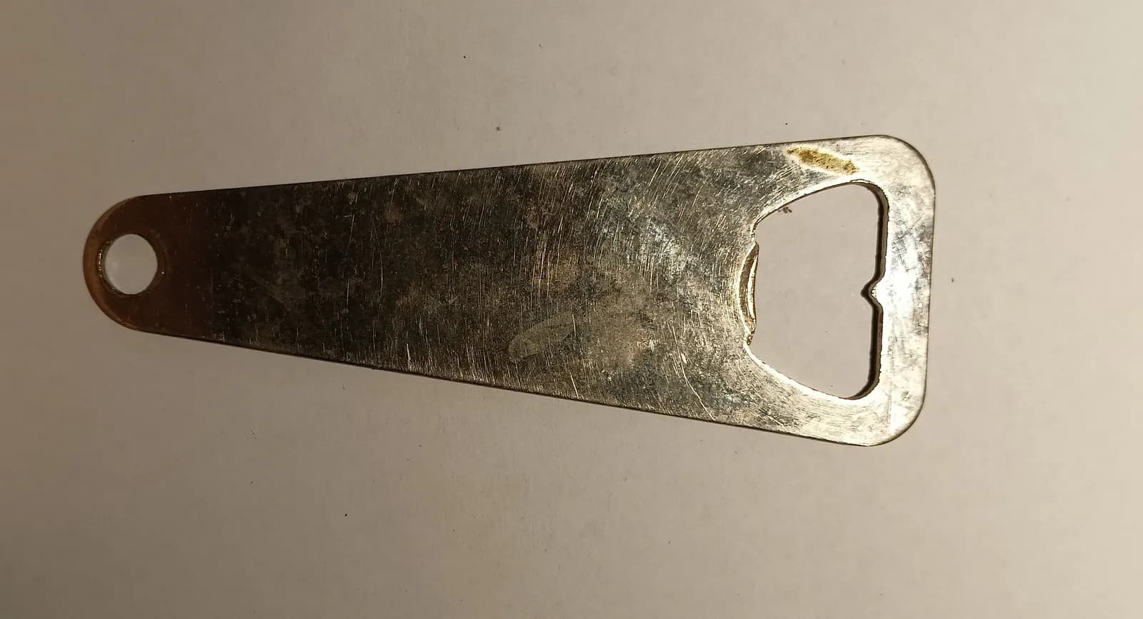 Décapsuleur plat en métal argenté, sans marque, avec un trou d'accroche à une extrémité et l'ouverture en forme de crochet à l'autre