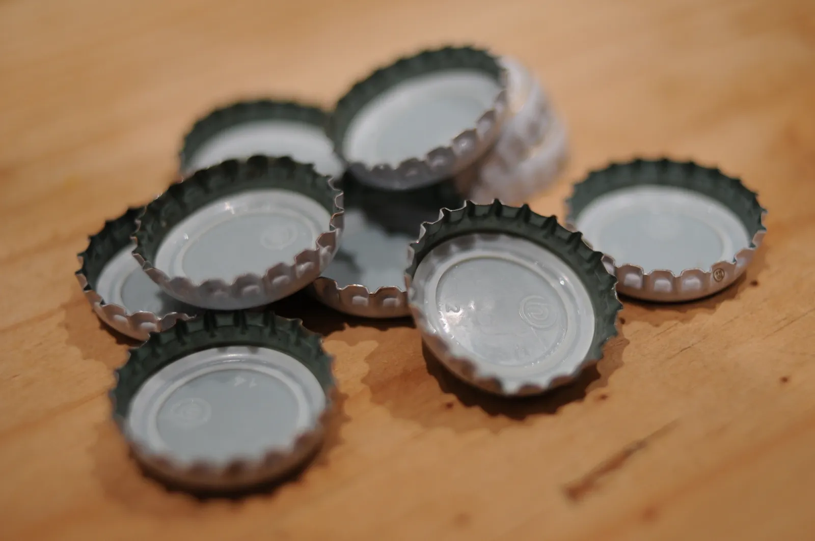 Plusieurs capsules de bière dentelées retournées sur une table en bois, leur joint intérieur blanc visible