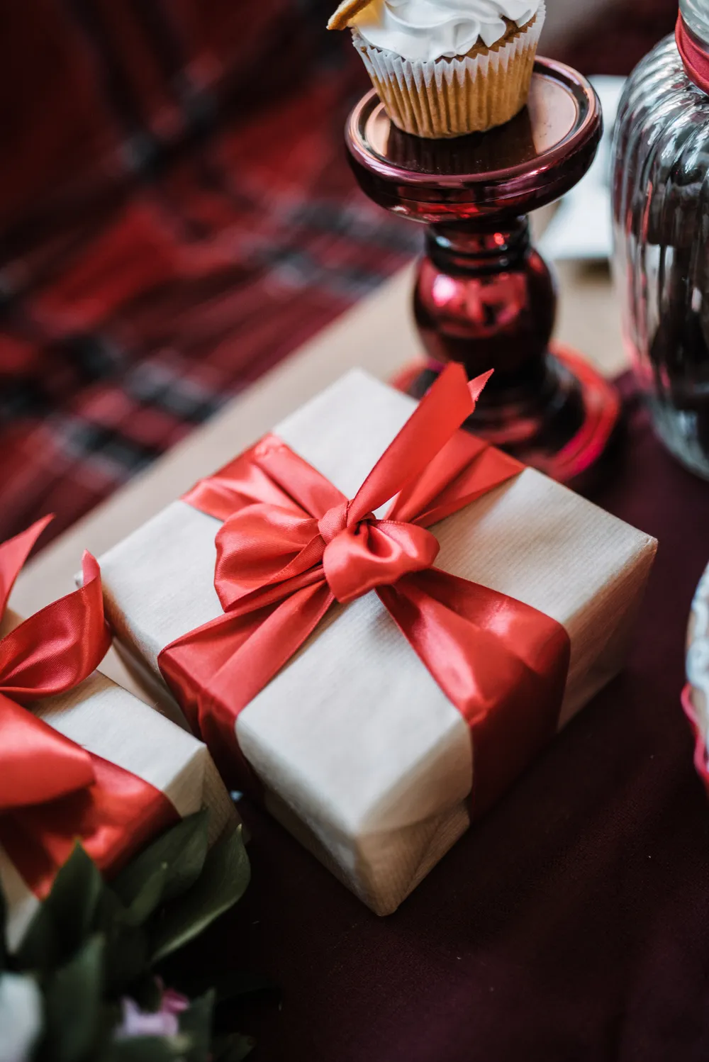 Paquet cadeau emballé dans du papier kraft clair et noué d'un large ruban rouge, posé sur une table de fête