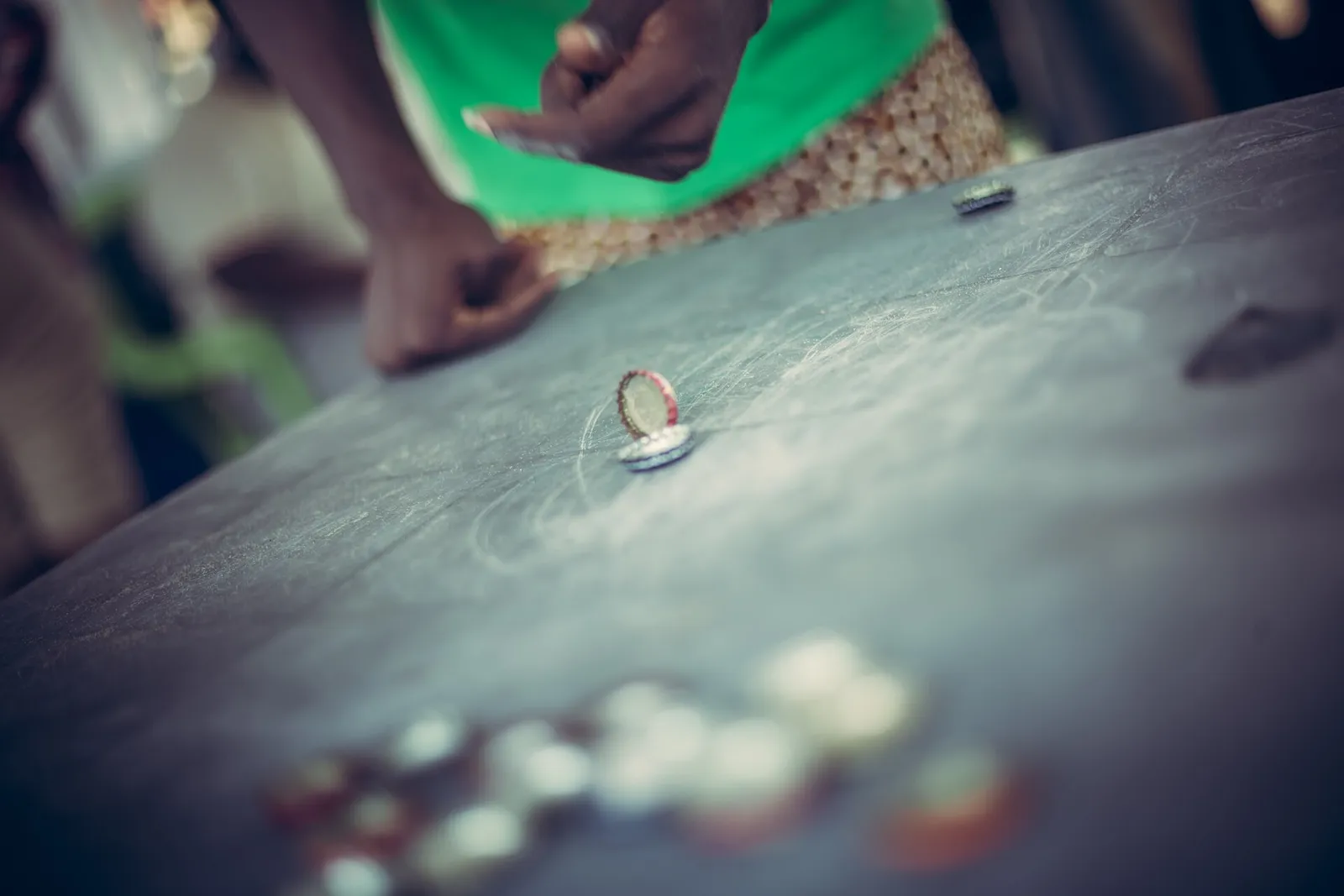 Partie de pichenette de capsules sur une table : une capsule retournée se pose sur une autre, d'autres capsules floues au premier plan
